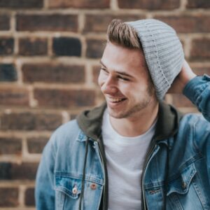 man holding the back of his head while smiling near brick wall